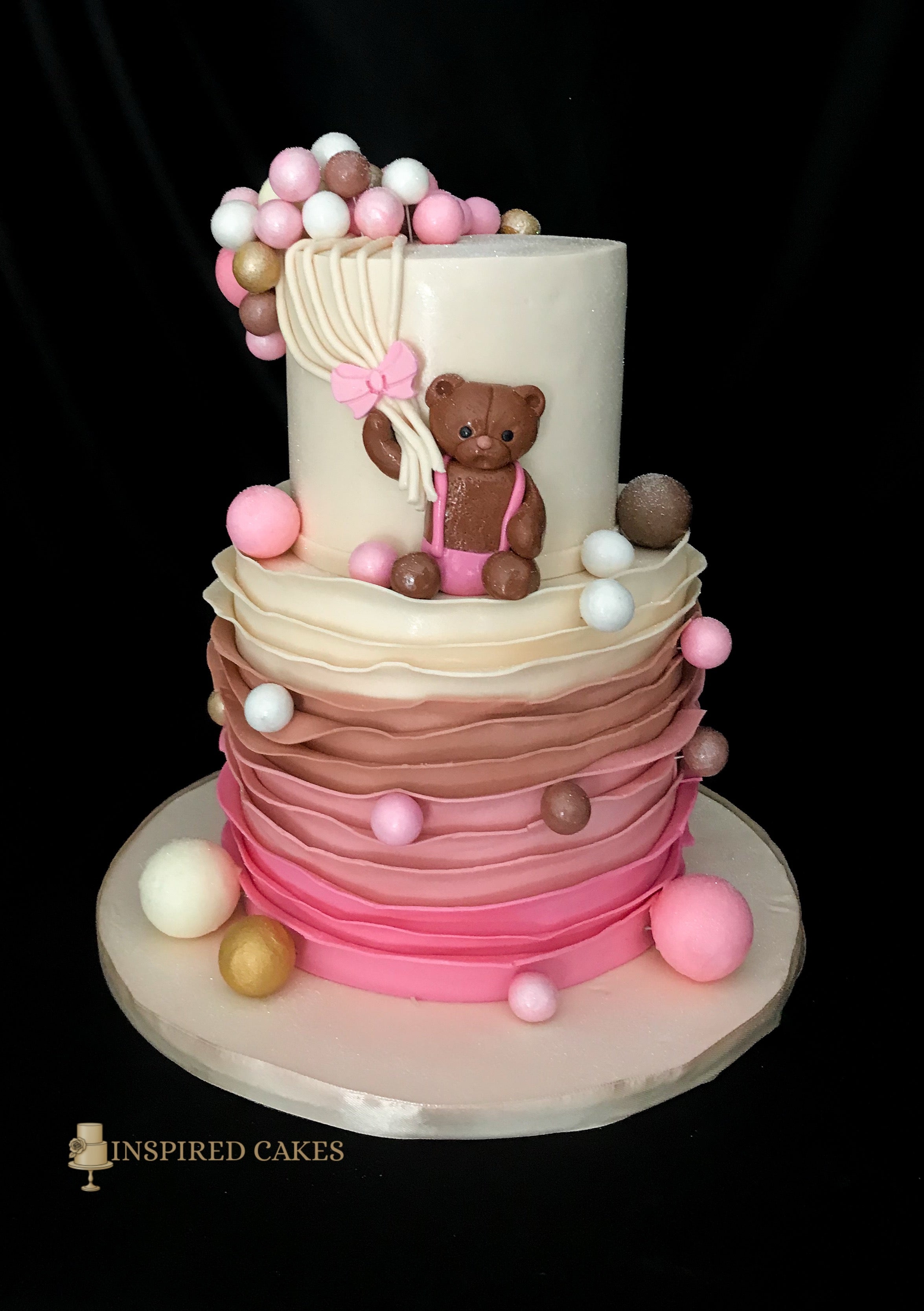 2-tiered cake with a teddy bear and balloons on a black background