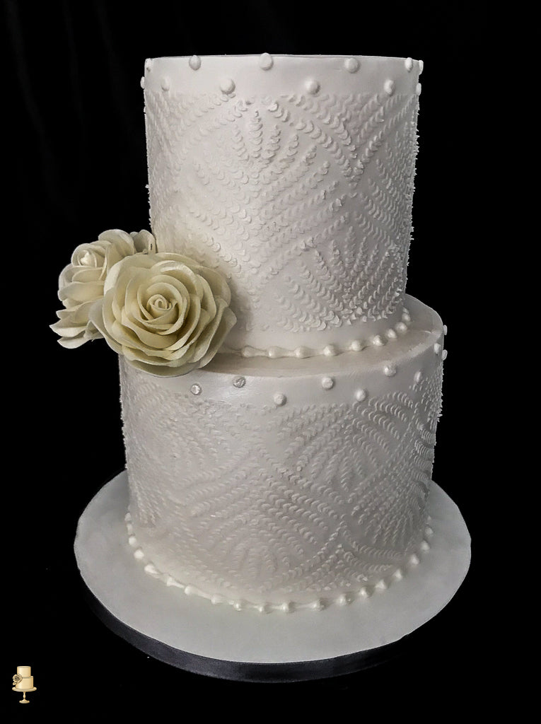 Two-tiered white wedding cake with lace patterns and a single white rose on a black background