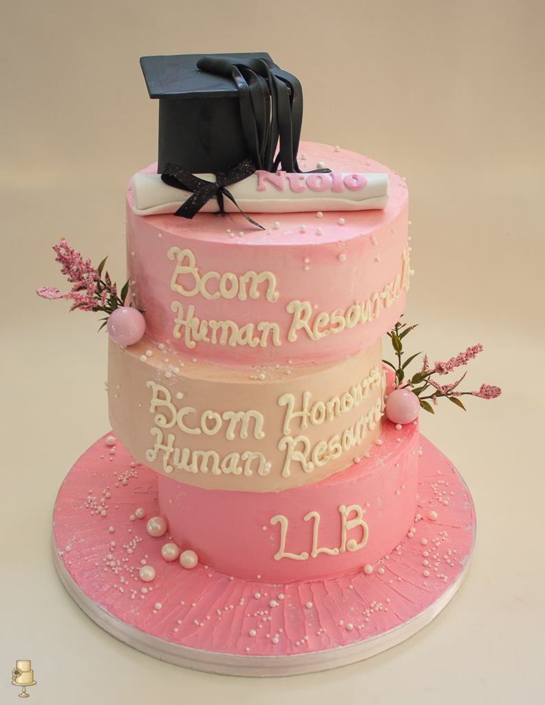 Graduation-themed cake with pink frosting, a black graduation cap, and scroll, on a beige background.